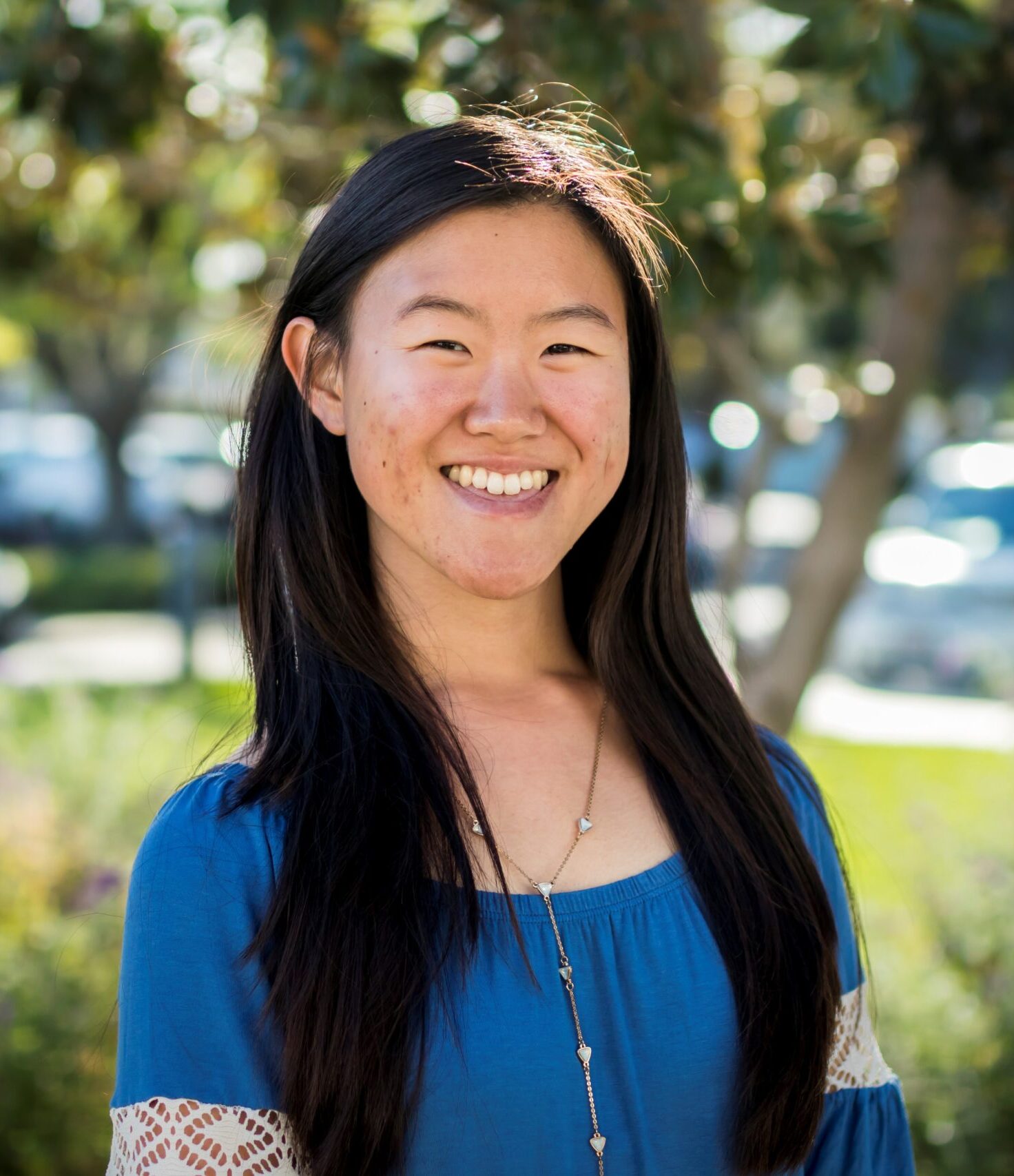 woman in blue dress wearing a necklace with trees and cars in background