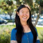 woman with black hair smiling and posing for camera in front of foliage