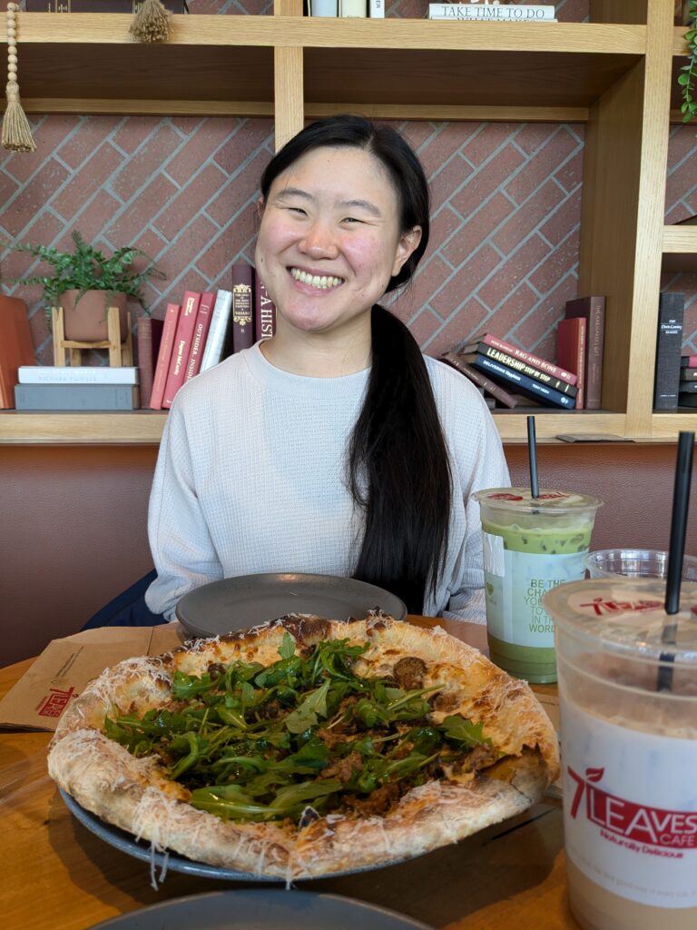 woman with black hair smiling in front of pizza and boba