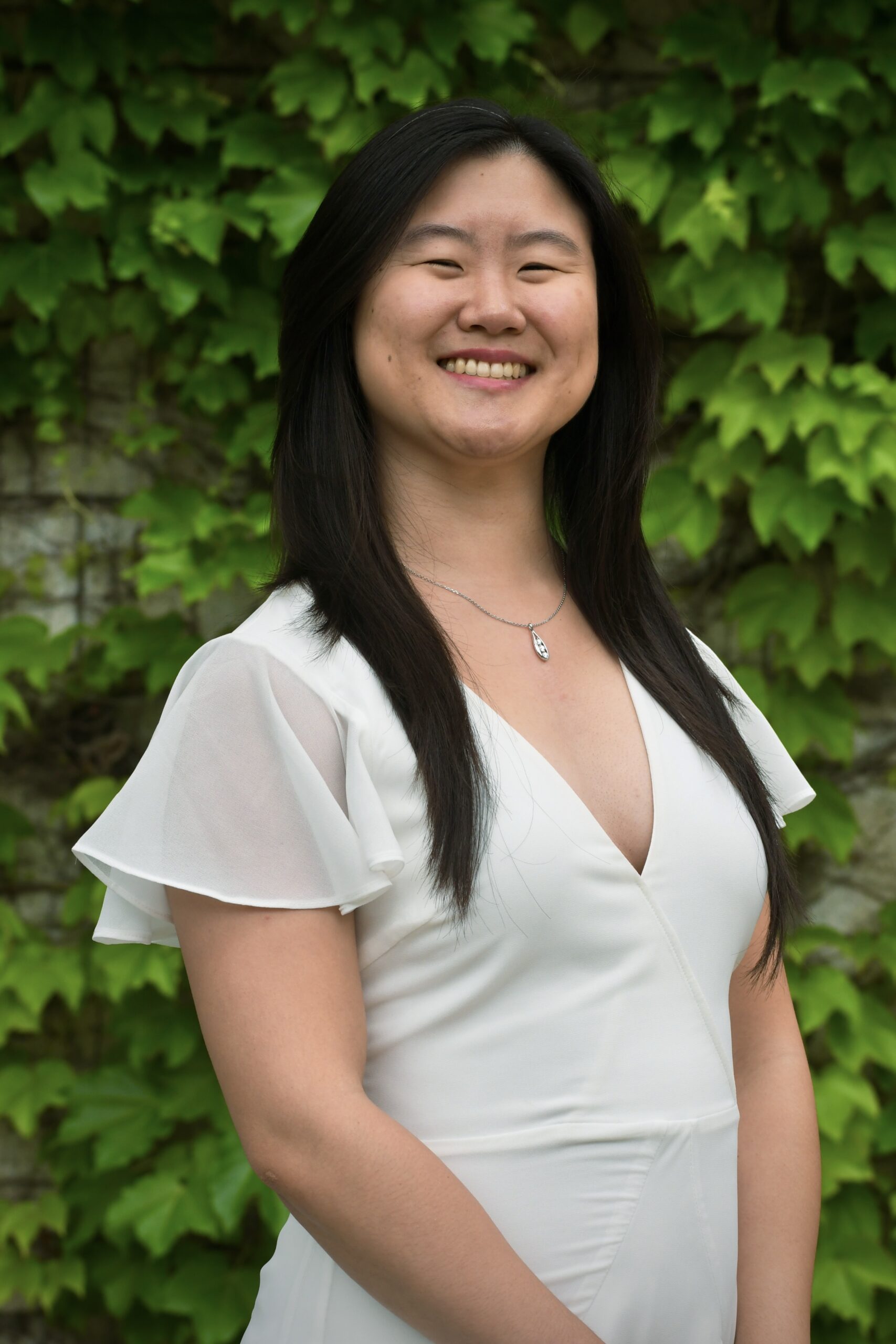 Woman with black hair posing in front of vines on a wall